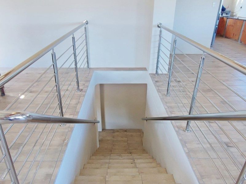 A staircase featuring modern stainless steel balustrades and tiled steps, connecting the upper level to the lower floor area.