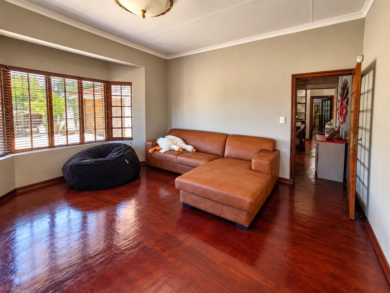 A well-maintained living room featuring polished wooden flooring, a large bay window with wooden blinds, and neutral wall tones.