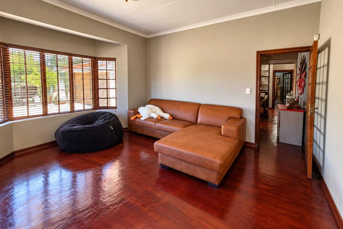 A well-maintained living room featuring polished wooden flooring, a large bay window with wooden blinds, and neutral wall tones.