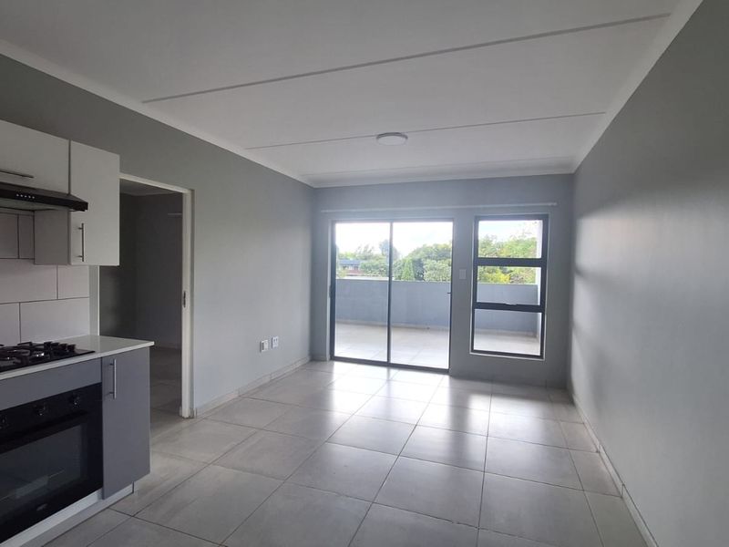 An open-plan living area featuring a modern kitchen with built-in appliances, tiled flooring, and sliding glass doors leading to a balcony.