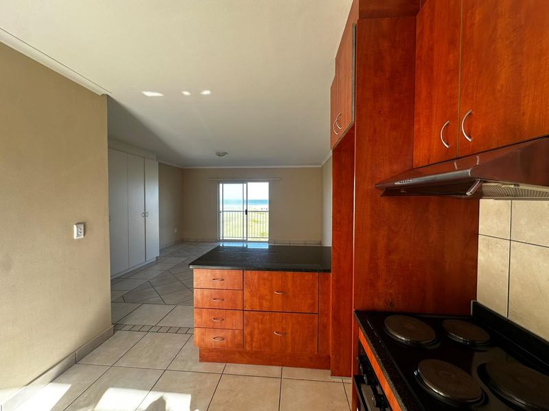 Open-plan kitchen and living area featuring wooden cabinetry, granite countertops, tiled flooring, and a sliding door leading to a balcony with ocean views.