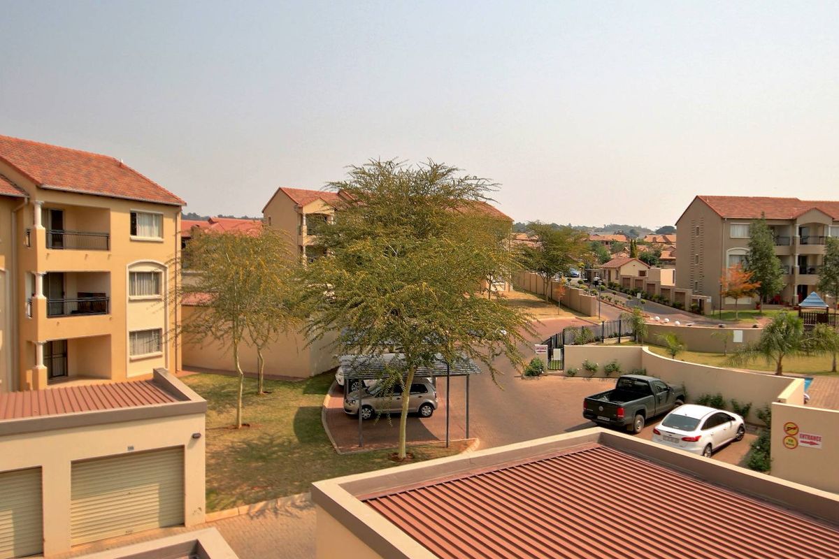 Elevated view of the apartment complex grounds, featuring paved driveways, covered parking bays, and landscaped garden areas between residential buildings.