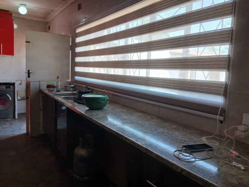 A functional kitchen featuring granite countertops, a stainless steel sink, and built-in cabinetry with modern roller blinds on the window.