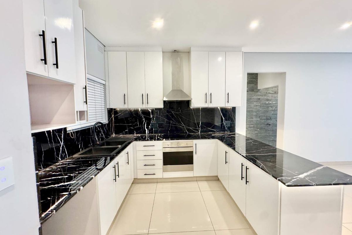 Modern kitchen featuring high-gloss white cabinetry, striking black marble-look countertops and splashback, stainless steel appliances, and sleek tiled flooring.