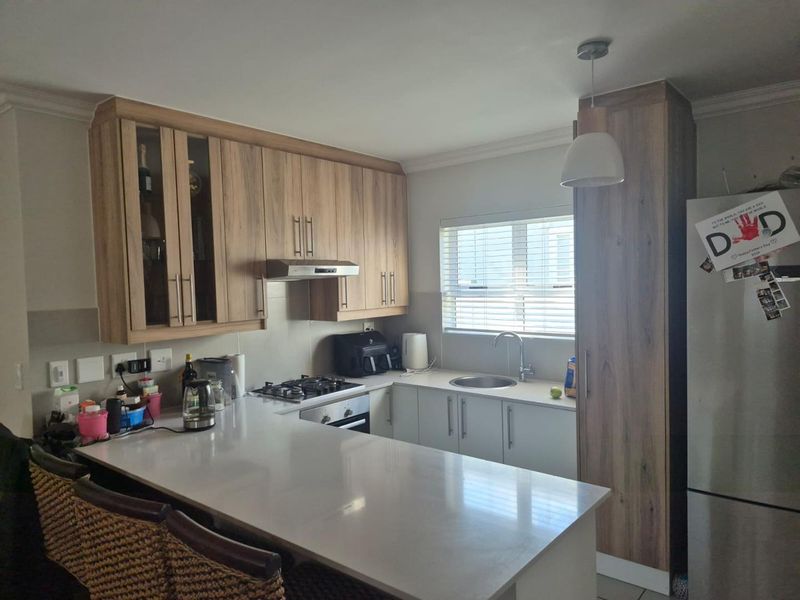 Modern kitchen featuring wood-look cabinetry, stone countertops, integrated gas hob, oven, and extractor fan with a breakfast bar and ample storage space.
