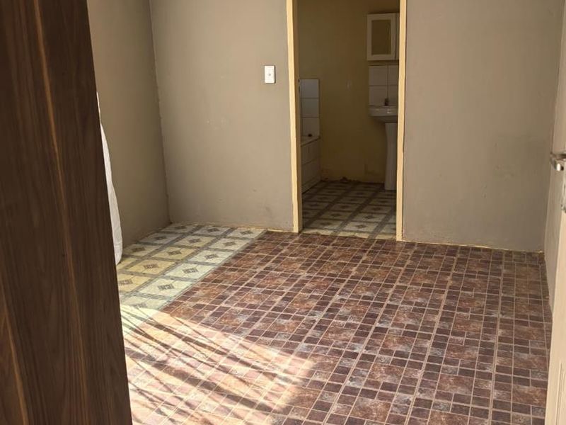An empty bedroom featuring vinyl flooring and neutral wall tones, with an adjoining bathroom visible through the doorway.