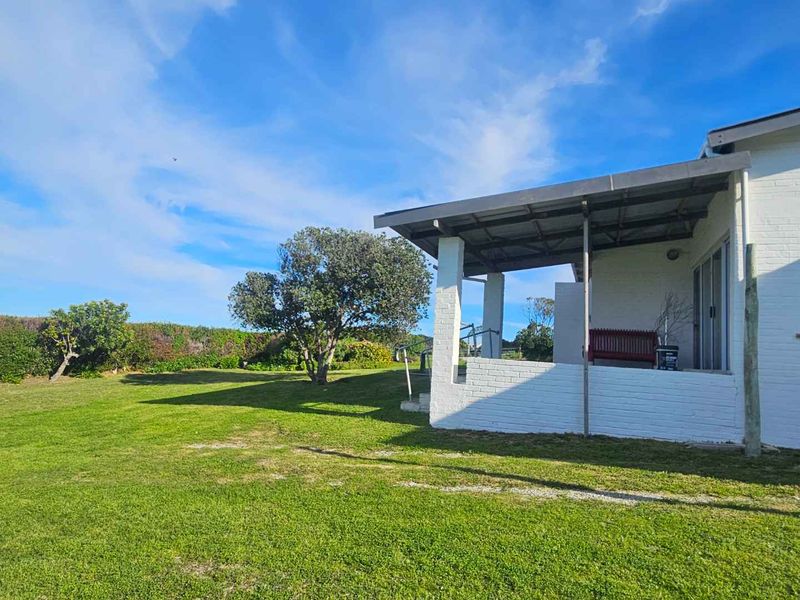 A rear view of the property featuring a covered patio area with painted brick pillars and sliding glass doors overlooking a spacious garden.