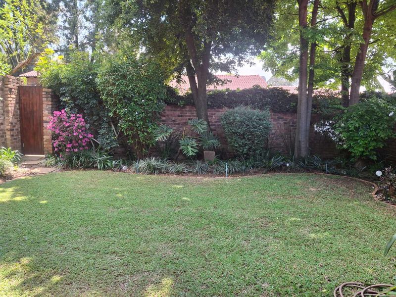A well-maintained private garden featuring a lush lawn, mature trees, and a secure brick boundary wall with a wooden access gate.