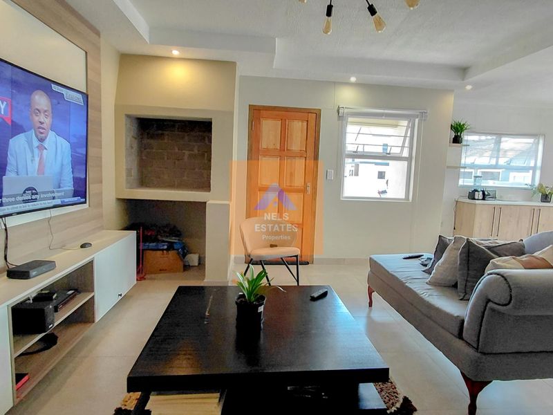 Open-plan living area featuring a built-in fireplace, tiled flooring, and a modern kitchen with light wood cabinetry.