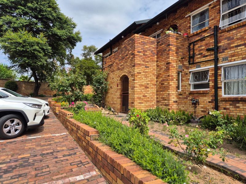 Front elevation of a face brick apartment building featuring a paved driveway, landscaped garden beds, and secure window treatments.