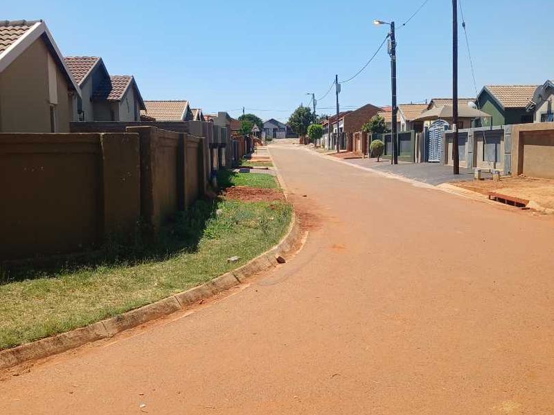 A view of a residential street featuring paved roads, concrete boundary walls, and typical suburban housing with tiled roofs.