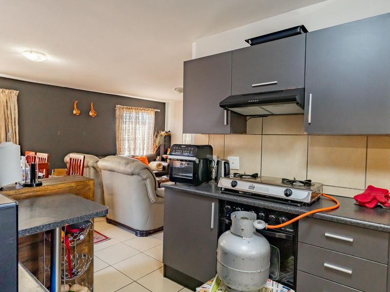Open-plan living area featuring a kitchen with dark cabinetry, gas hob, extractor fan, and tiled flooring, seamlessly flowing into the adjacent living space.