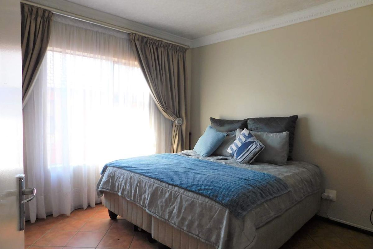 A well-lit bedroom featuring tiled flooring, decorative ceiling cornicing, and a large window with curtain tracks.