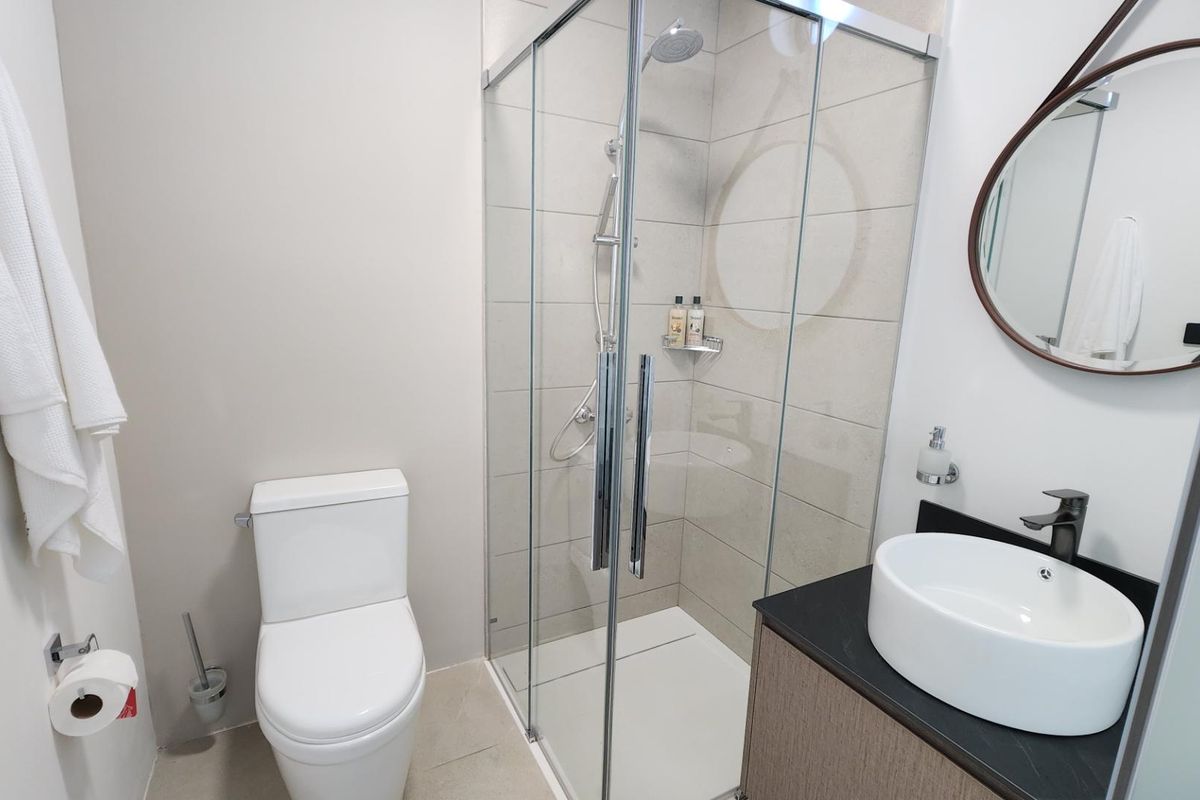 Modern bathroom featuring a glass-enclosed shower, a contemporary vessel sink vanity with a dark countertop, and a wall-mounted toilet.