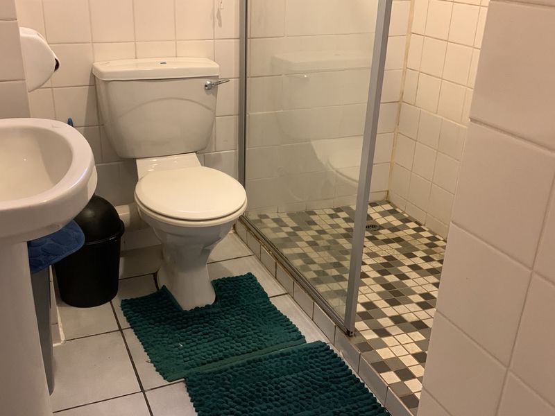 A functional bathroom featuring a pedestal basin, toilet, and a glass-enclosed shower with tiled finishes throughout.