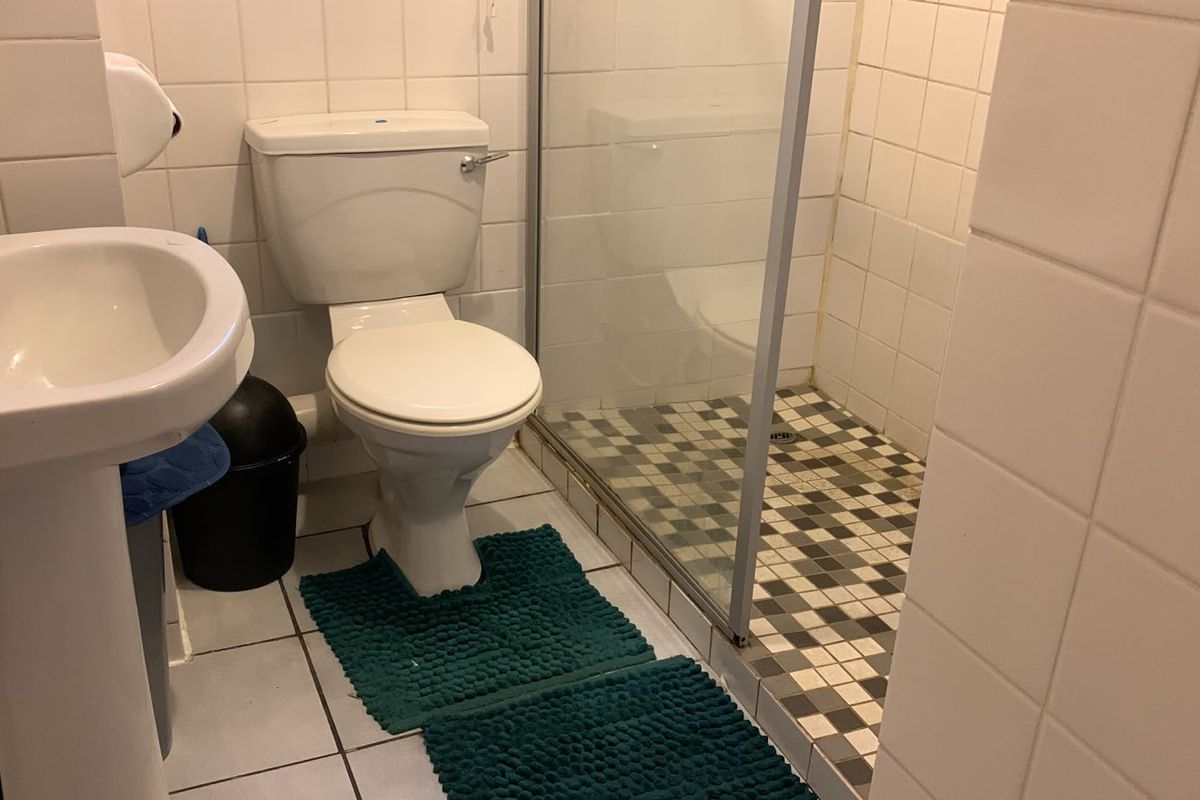 A functional bathroom featuring a pedestal basin, toilet, and a glass-enclosed shower with tiled finishes throughout.