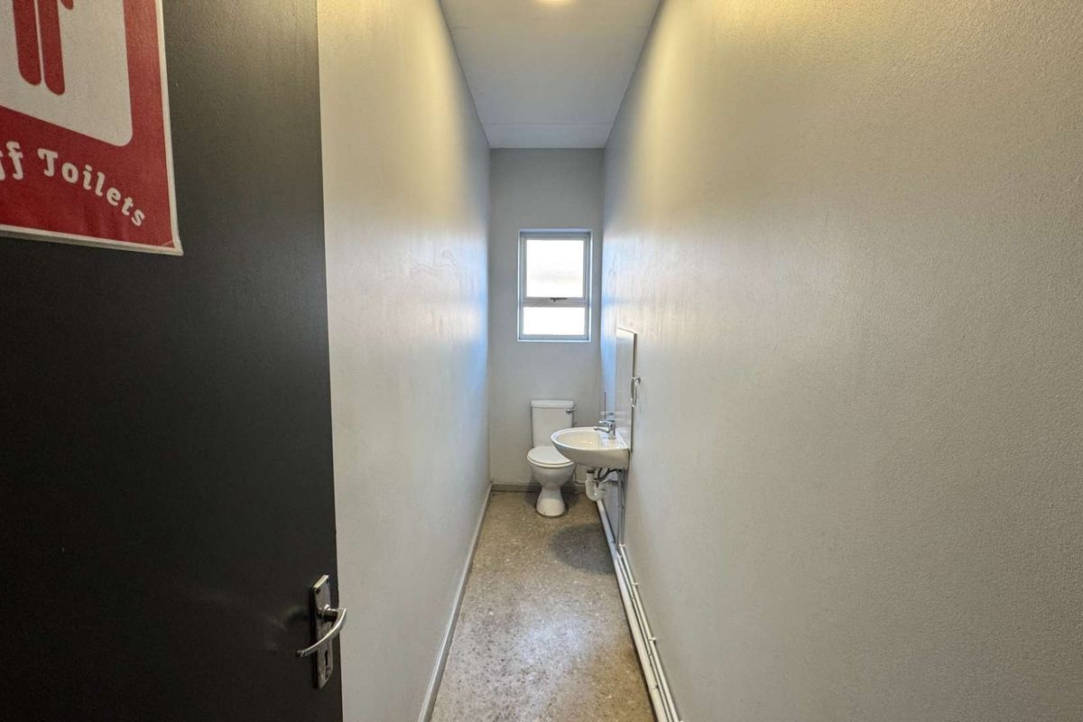 A functional staff restroom featuring a toilet, wall-mounted basin, and window, finished with simple wall surfaces and flooring.