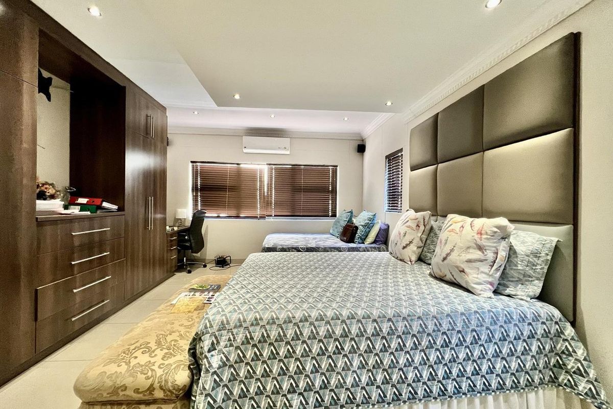 Spacious bedroom featuring extensive built-in cabinetry, a large upholstered headboard, recessed ceiling lighting, and a wall-mounted air conditioning unit.