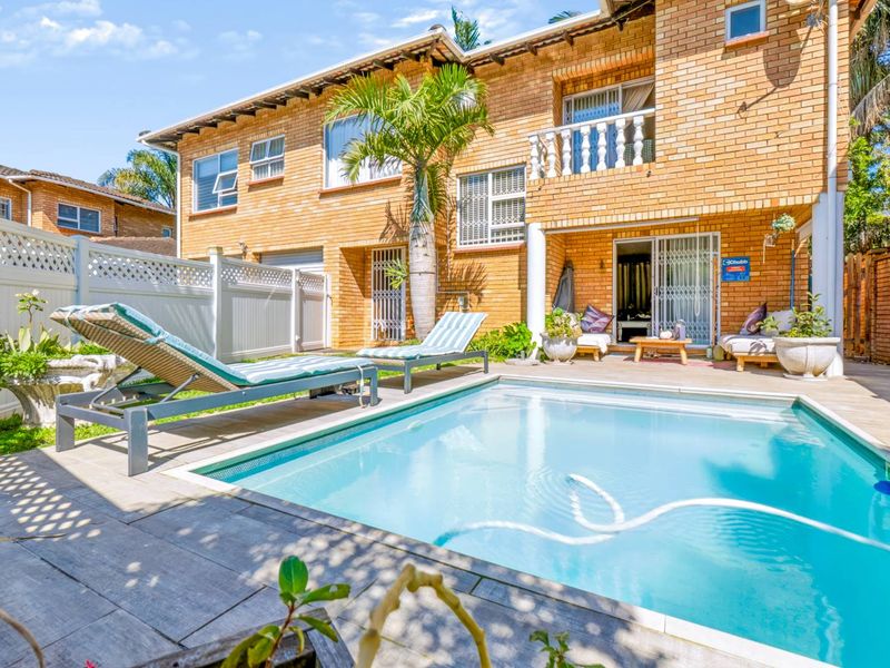 A private backyard featuring a swimming pool, paved patio area, and a two-story brick townhouse facade with a balcony.