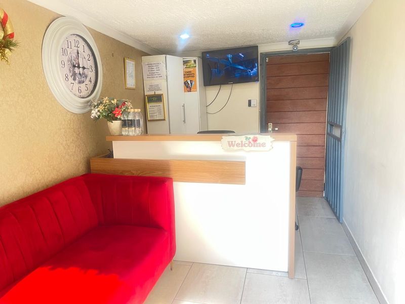 A functional guest house reception area featuring a built-in service counter, tiled flooring, and a secure entrance door.