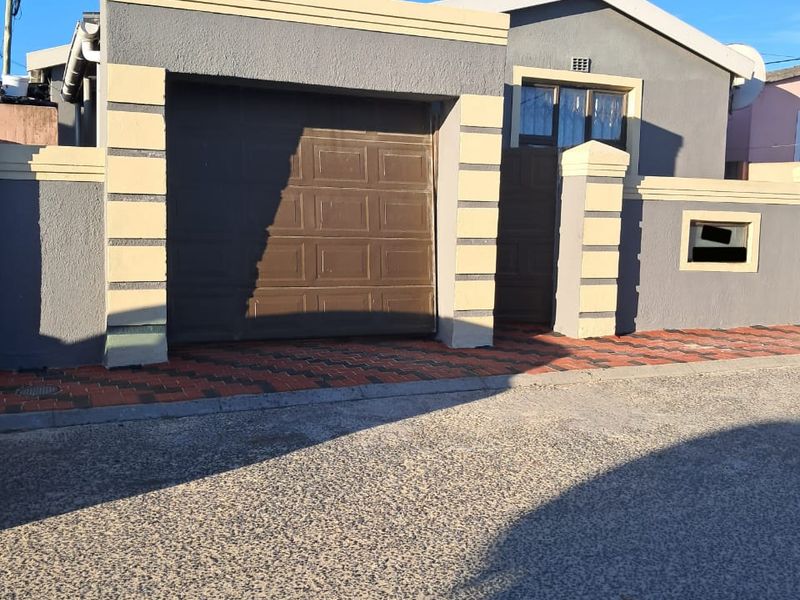 Front elevation of a residential property featuring a single garage, pedestrian gate, and paved driveway area.