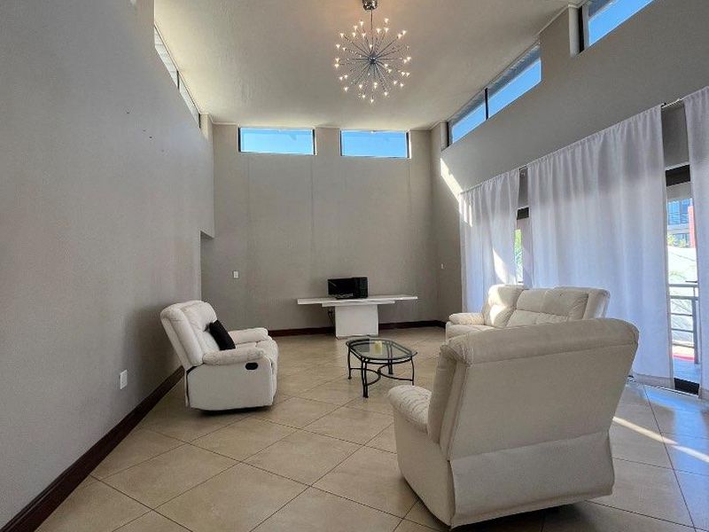 Spacious living room featuring high ceilings, abundant natural light from clerestory windows, tiled flooring, and direct access to an outdoor area.