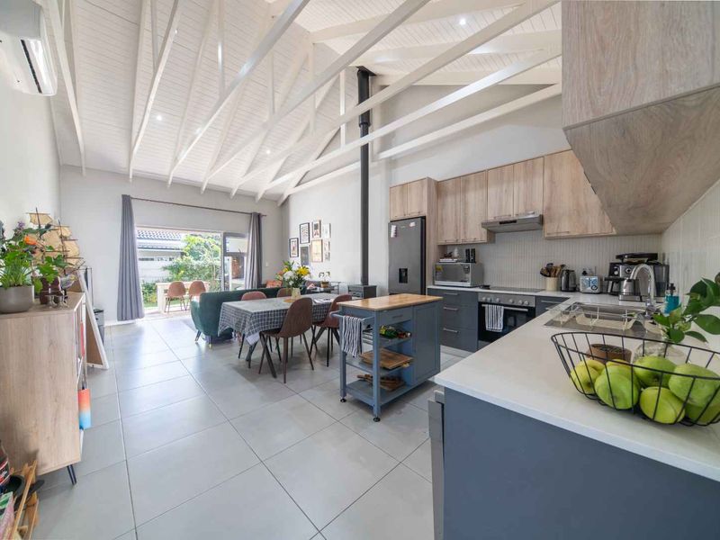 Spacious open-plan living and kitchen area featuring vaulted ceilings with exposed rafters, a modern wood-burning fireplace, and seamless flow to the outdoor patio.