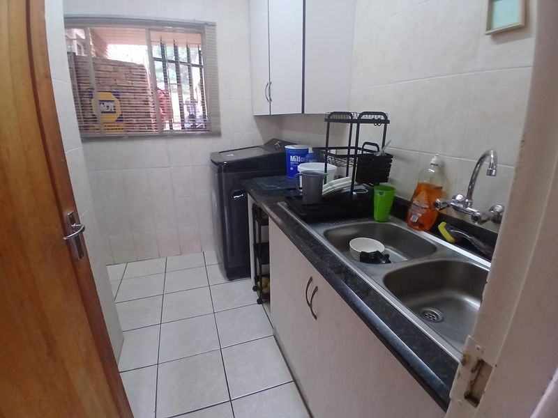 A functional laundry room featuring tiled walls and flooring, built-in cabinetry, and a double stainless steel sink with a window for natural light.