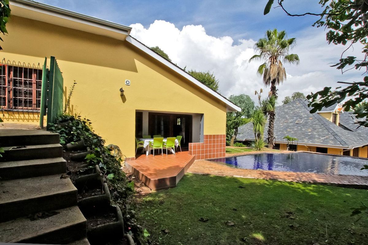 Rear exterior view featuring a swimming pool, tiled patio area, and concrete stairs leading to the garden.