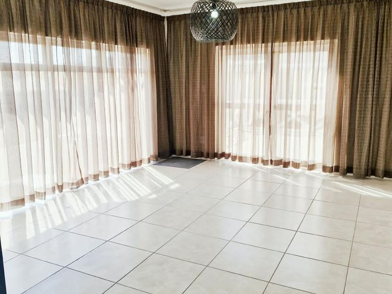 A bright, empty living area featuring large sliding glass doors with floor-to-ceiling curtains and neutral tiled flooring.