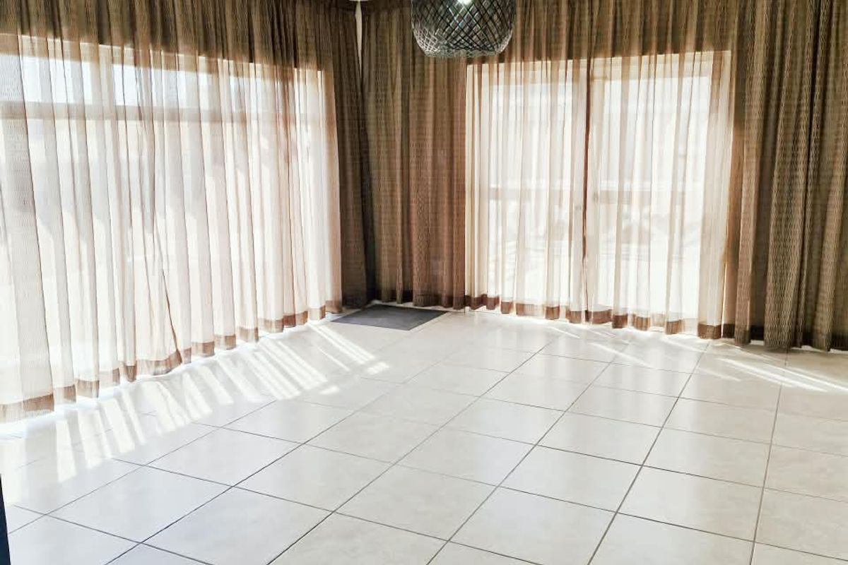 A bright, empty living area featuring large sliding glass doors with floor-to-ceiling curtains and neutral tiled flooring.