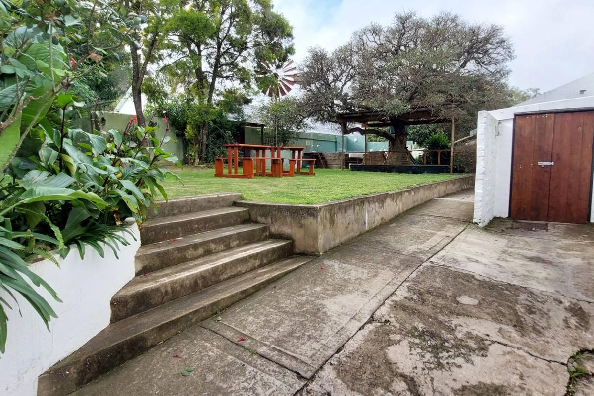 A rear garden area featuring a raised lawn, concrete retaining wall, paved walkway, and a wooden storage shed.