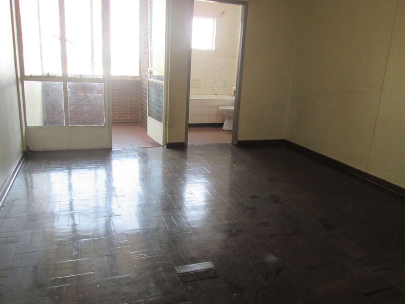 An empty living room featuring original parquet flooring, with direct access to an attached balcony and a view into the adjacent bathroom.