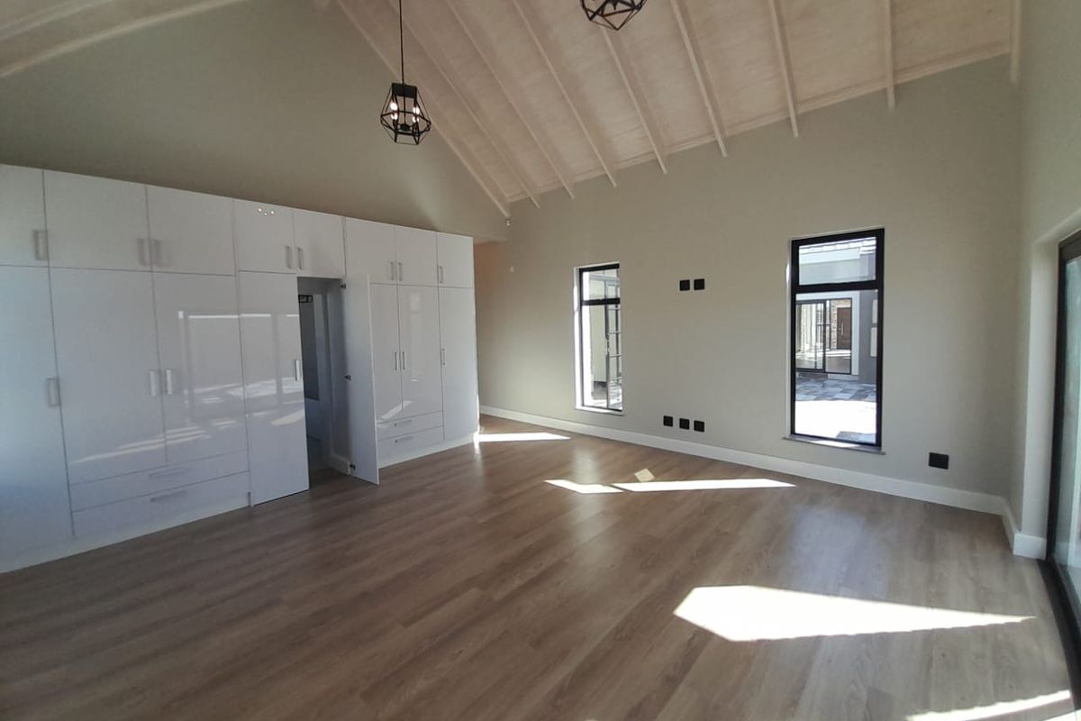 Spacious bedroom featuring high vaulted ceilings, light wood-look flooring, and extensive built-in white cabinetry with integrated storage.