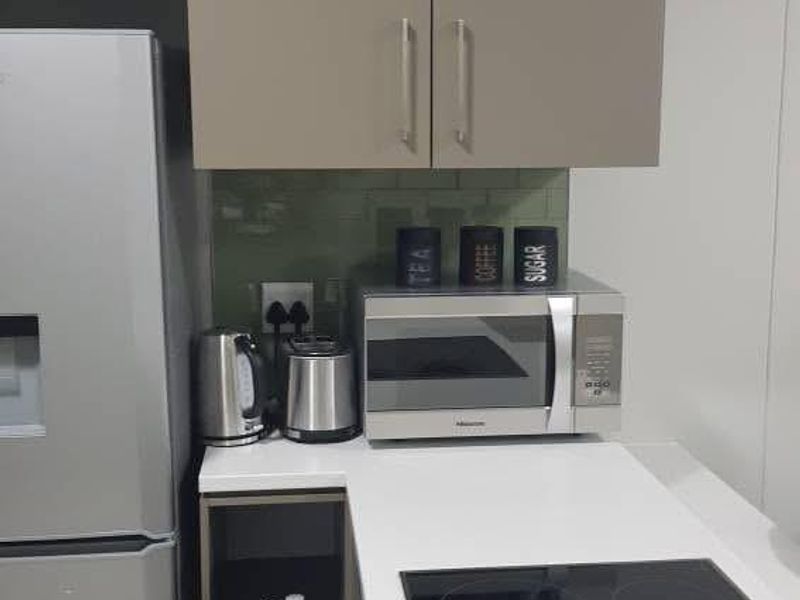 A compact, modern kitchen featuring sleek grey cabinetry, white quartz countertops, and a built-in electric induction cooktop with an integrated oven.