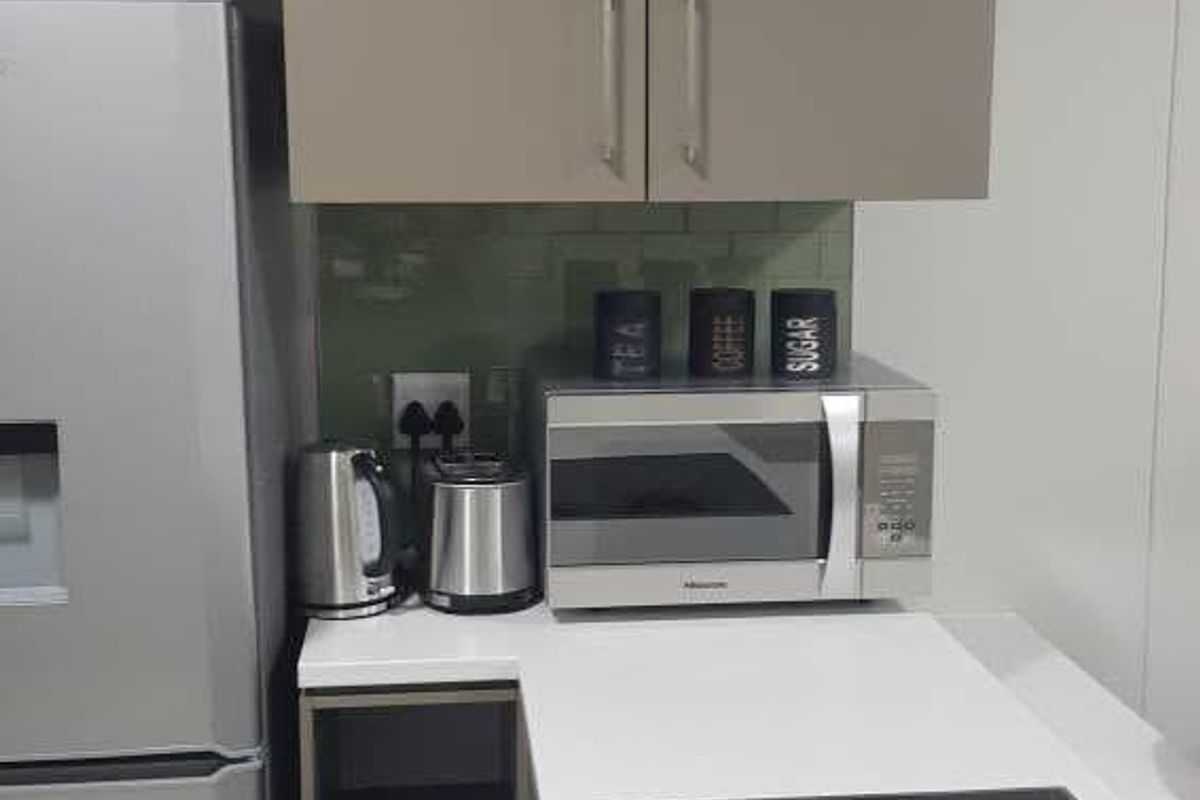 A compact, modern kitchen featuring sleek grey cabinetry, white quartz countertops, and a built-in electric induction cooktop with an integrated oven.