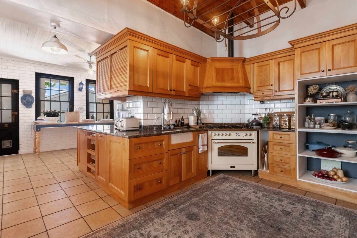 A rustic farmhouse kitchen featuring warm timber cabinetry, a classic farmhouse sink, subway tile backsplash, and a professional-style freestanding oven.