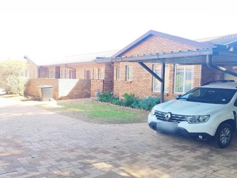 Front exterior view of a brick townhouse featuring a paved driveway, carport, and low-maintenance garden area.
