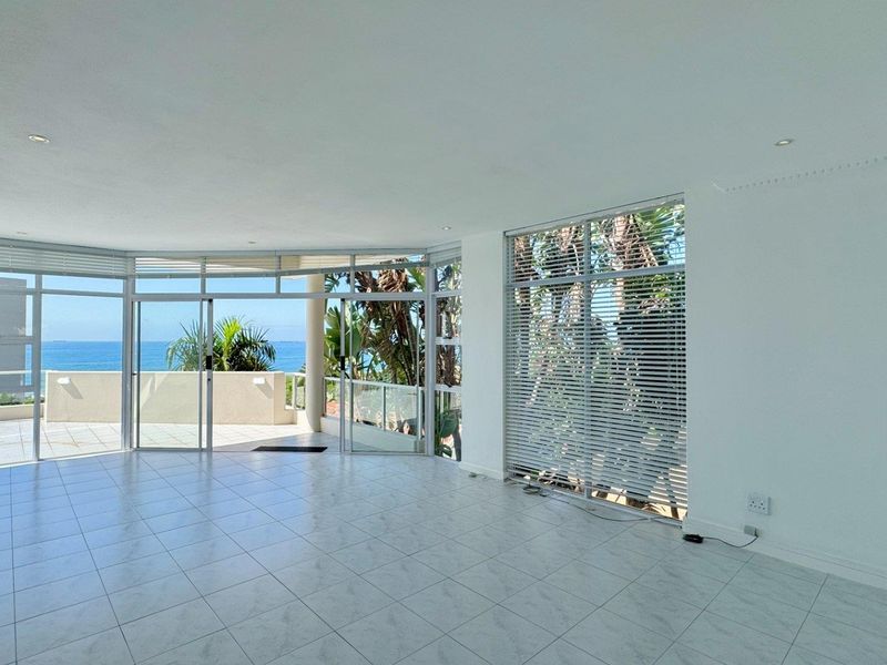 Spacious, light-filled living area featuring large windows, tiled floors, and direct access to a balcony with ocean views.