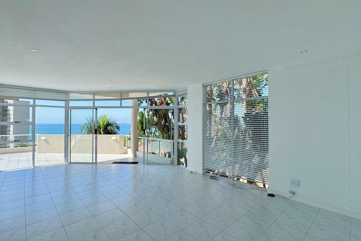 Spacious, light-filled living area featuring large windows, tiled floors, and direct access to a balcony with ocean views.