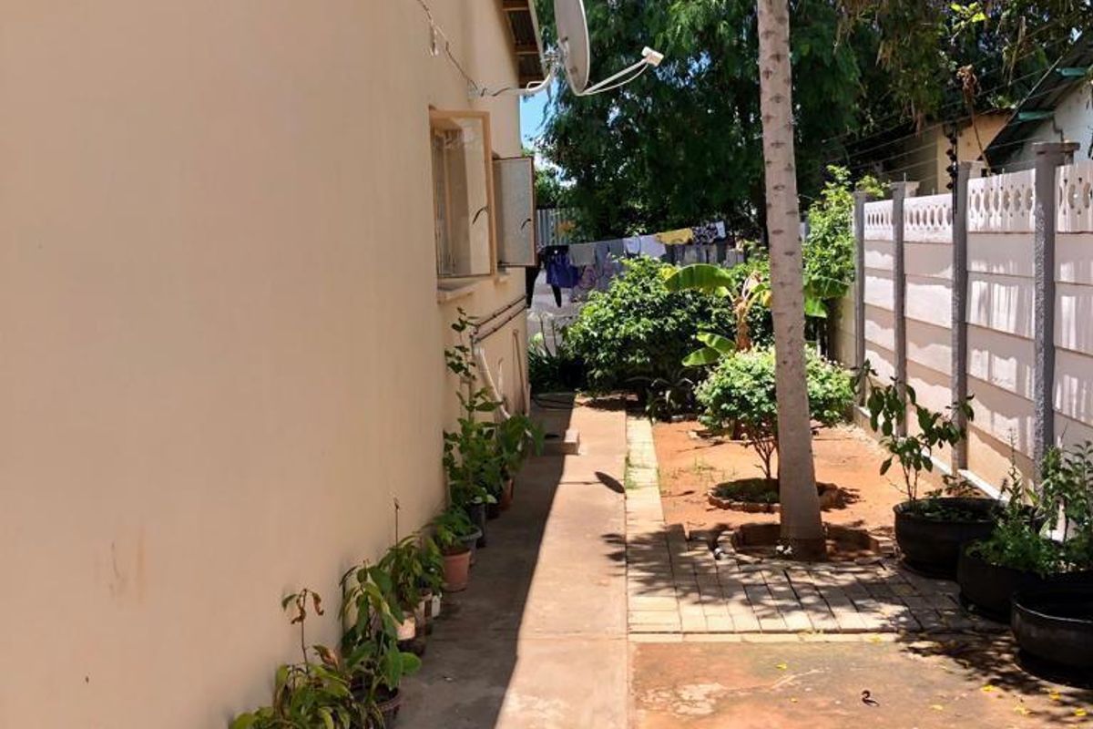 A view of the rear exterior of the property featuring a paved walkway, boundary wall, and exterior wall with a satellite dish.