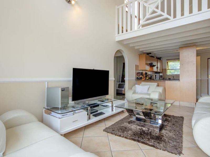 Open-plan living area featuring a mezzanine level, tiled flooring, and an integrated kitchen space with wooden cabinetry.
