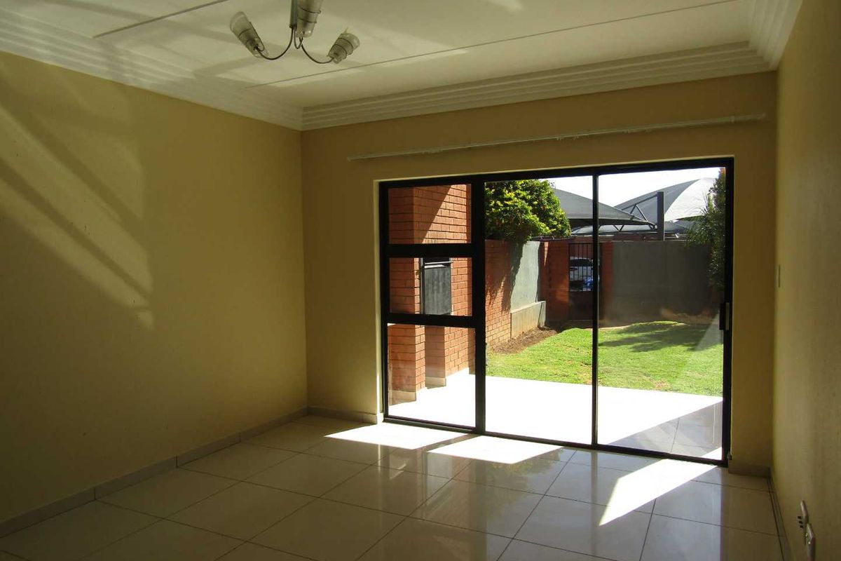 An empty living room featuring tiled flooring, a ceiling light fixture, and large sliding glass doors providing direct access to a private garden area.
