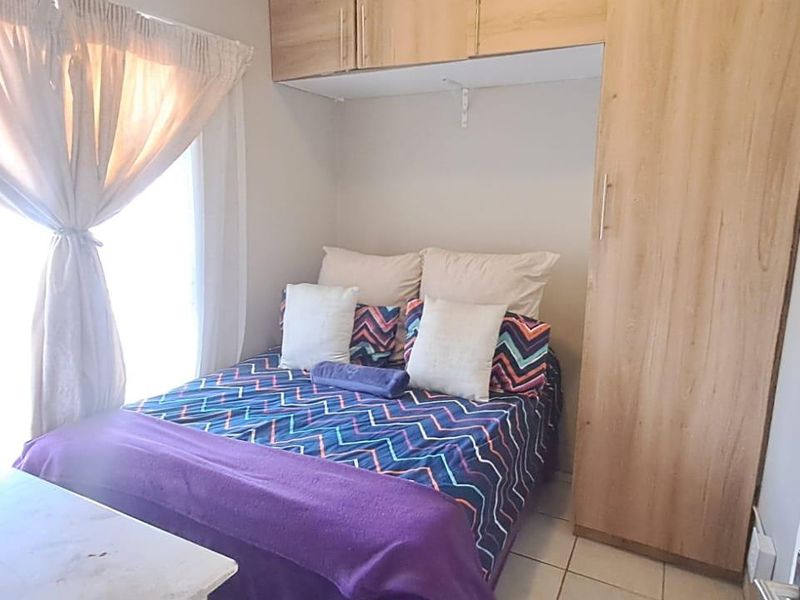 A compact bedroom featuring built-in wooden wardrobes with overhead storage and tiled flooring.