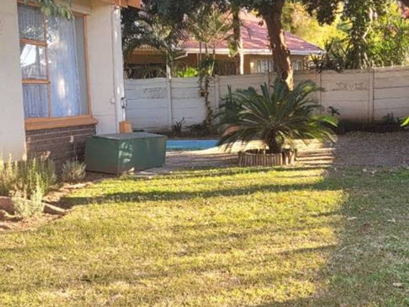 A private backyard garden featuring a lawn area, mature trees, and a swimming pool enclosed by a precast concrete boundary wall.