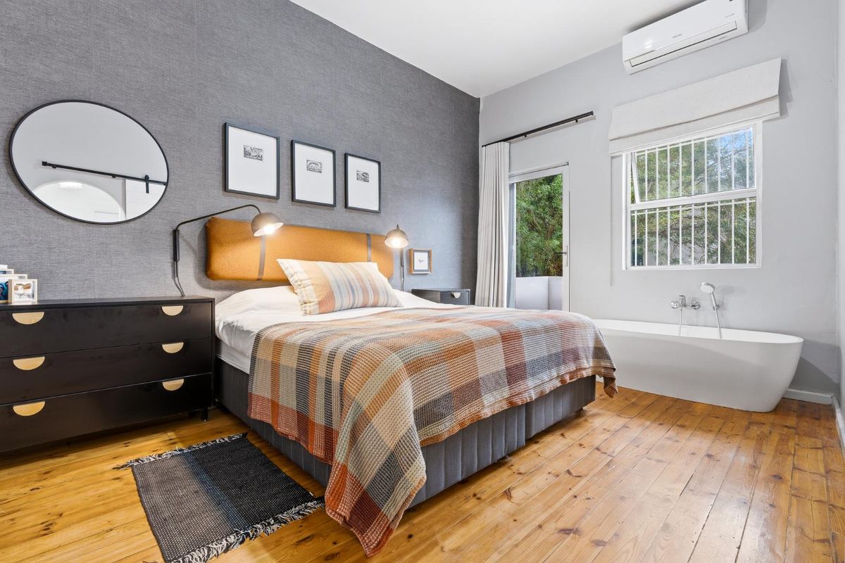 A well-appointed bedroom featuring hardwood flooring, a textured feature wall, a split-system air conditioner, and a unique integrated freestanding bathtub.