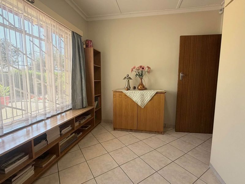A bedroom featuring tiled flooring, built-in shelving, and a window with security bars, offering a functional and well-maintained living space.