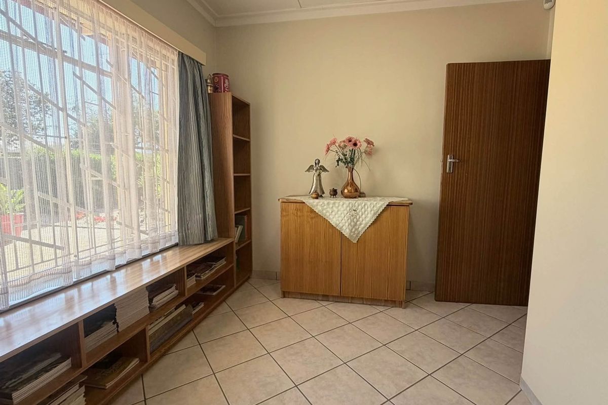A bedroom featuring tiled flooring, built-in shelving, and a window with security bars, offering a functional and well-maintained living space.