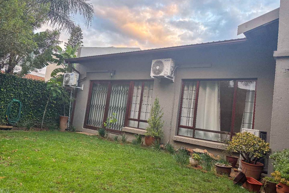 Rear view of the property featuring a private garden, lawn area, and exterior wall with mounted air conditioning units and security gates.