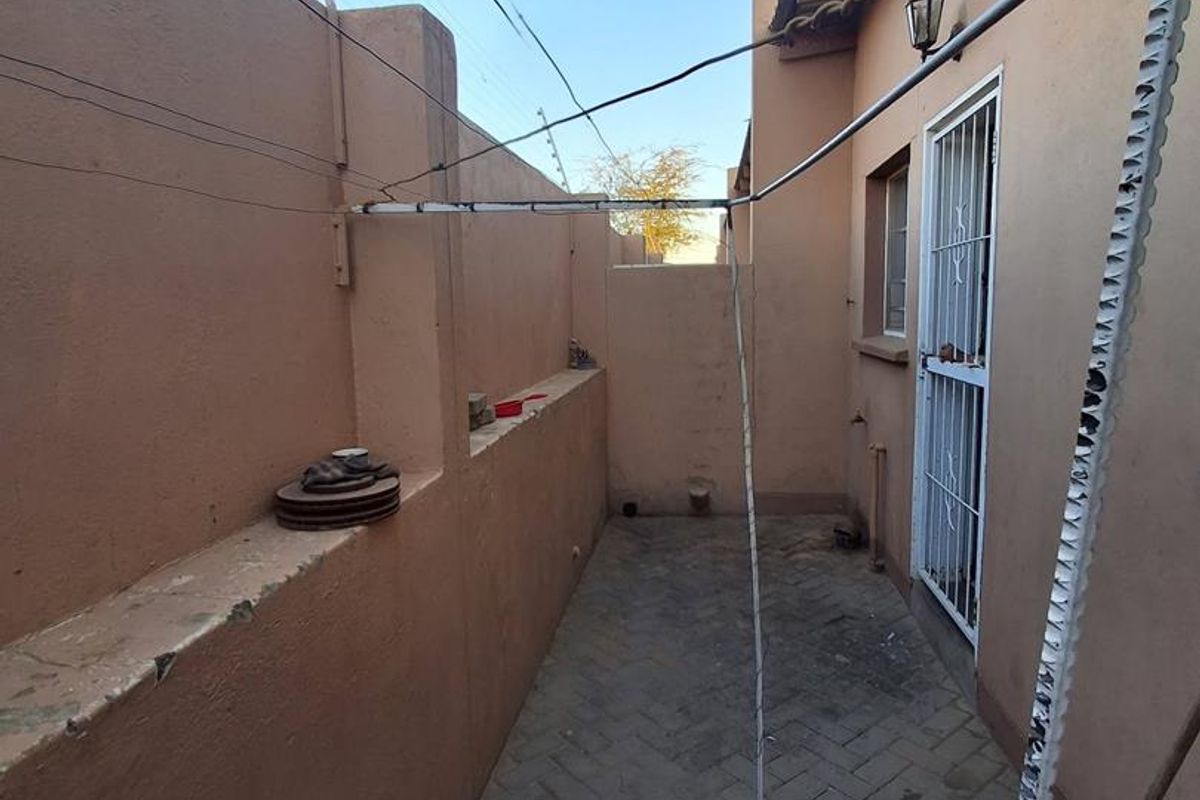 A narrow rear courtyard featuring paved flooring, perimeter wall with electric fencing, and a security gate providing access to the property.